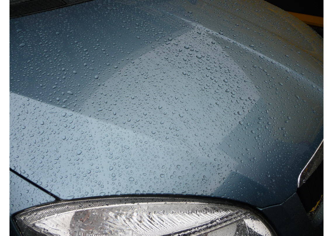 Hellblaue Motorhaube mit Wassertropfen.